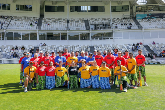 A group of people in red and yellow shirts standing together on a grass field in front of a grandstand. 